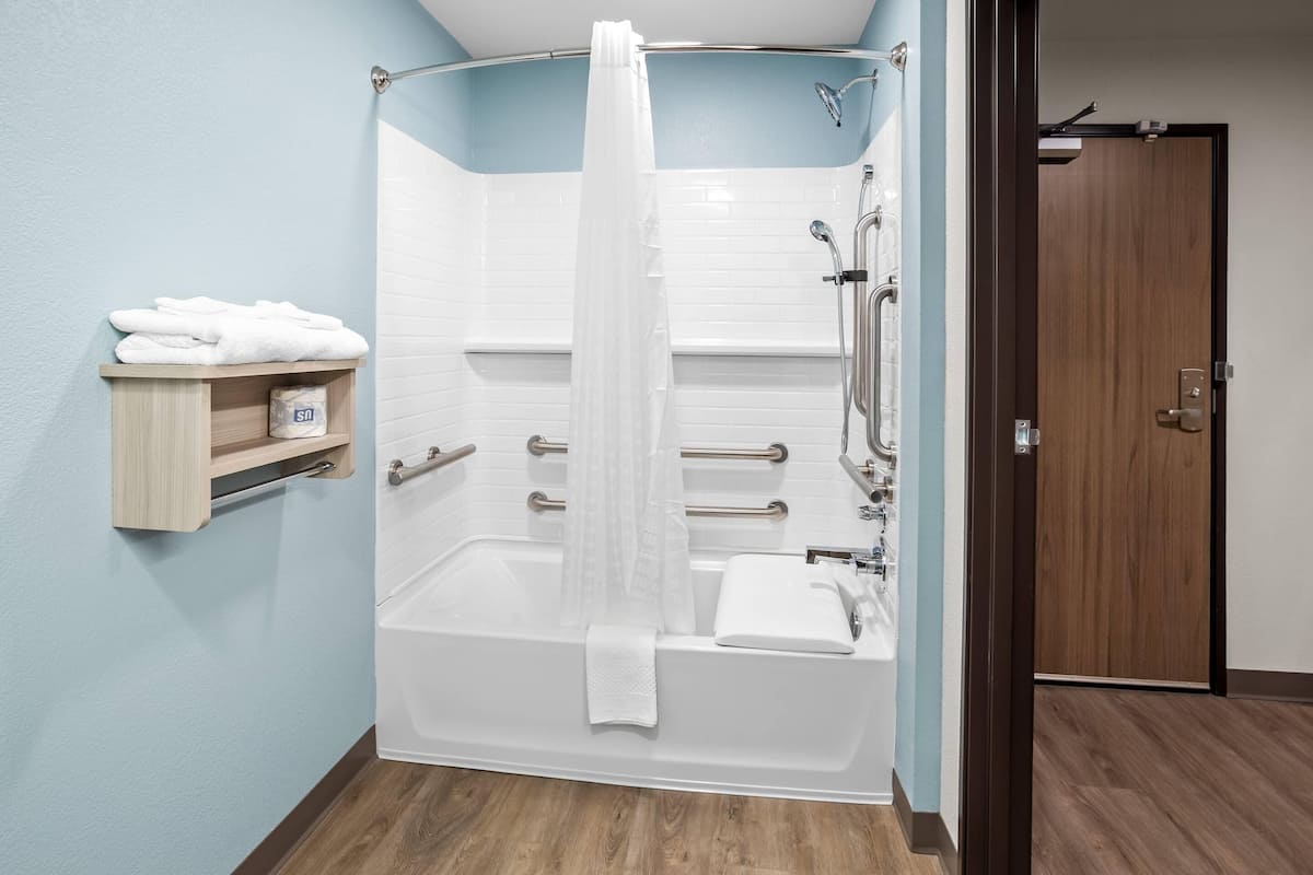 Een moderne badkamer met een inloopdouche, een bad en een toilet. Er is een handdoekrek met handdoeken en een plank met toiletartikelen.