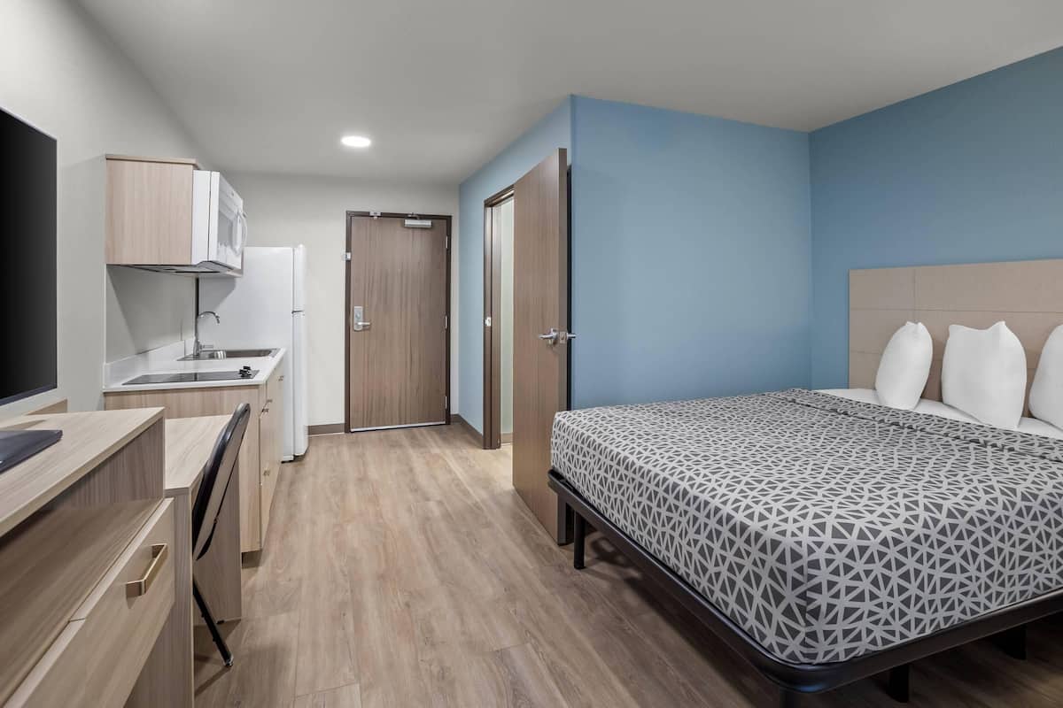 Een slaapkamer met een bed, een bureau, een kitchenette en een deur naar een andere kamer.