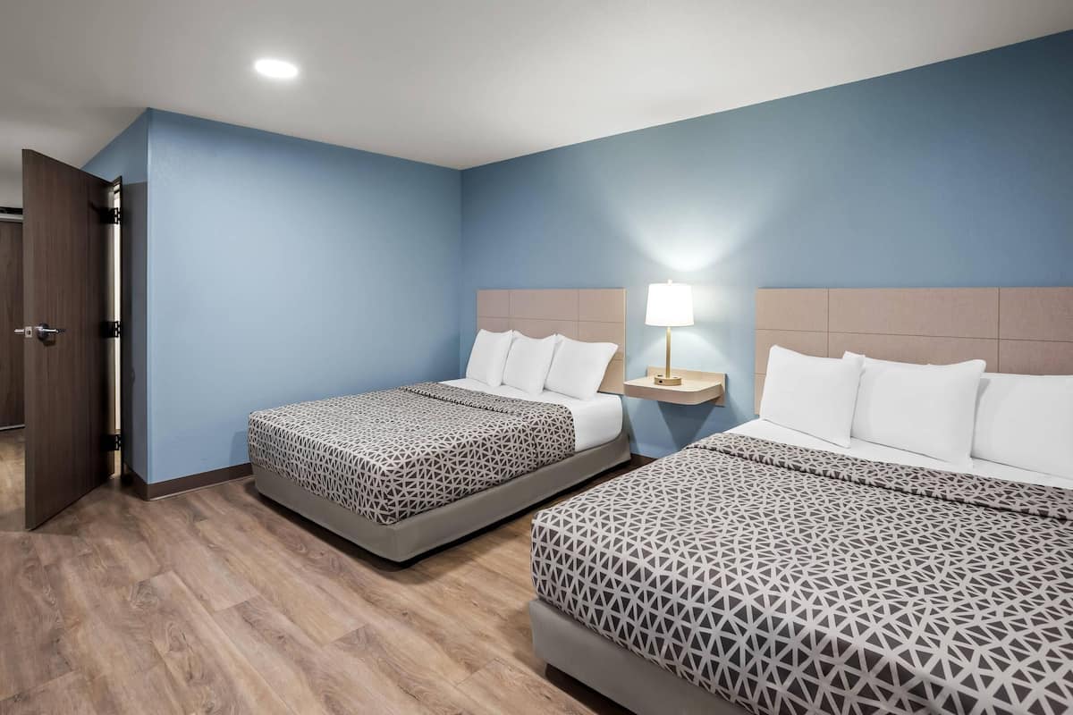 Een hotelkamer met twee bedden, een nachtkastje met een lamp en een houten deur.