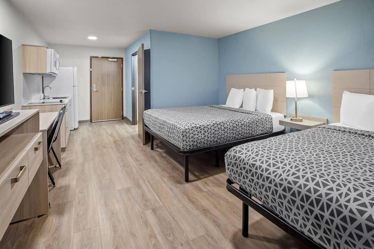 Een hotelkamer met twee bedden, een bureau, een kitchenette en een televisie.