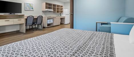 Una habitación de hotel moderna con cama, escritorio, silla, televisor, microondas y kitchenette.