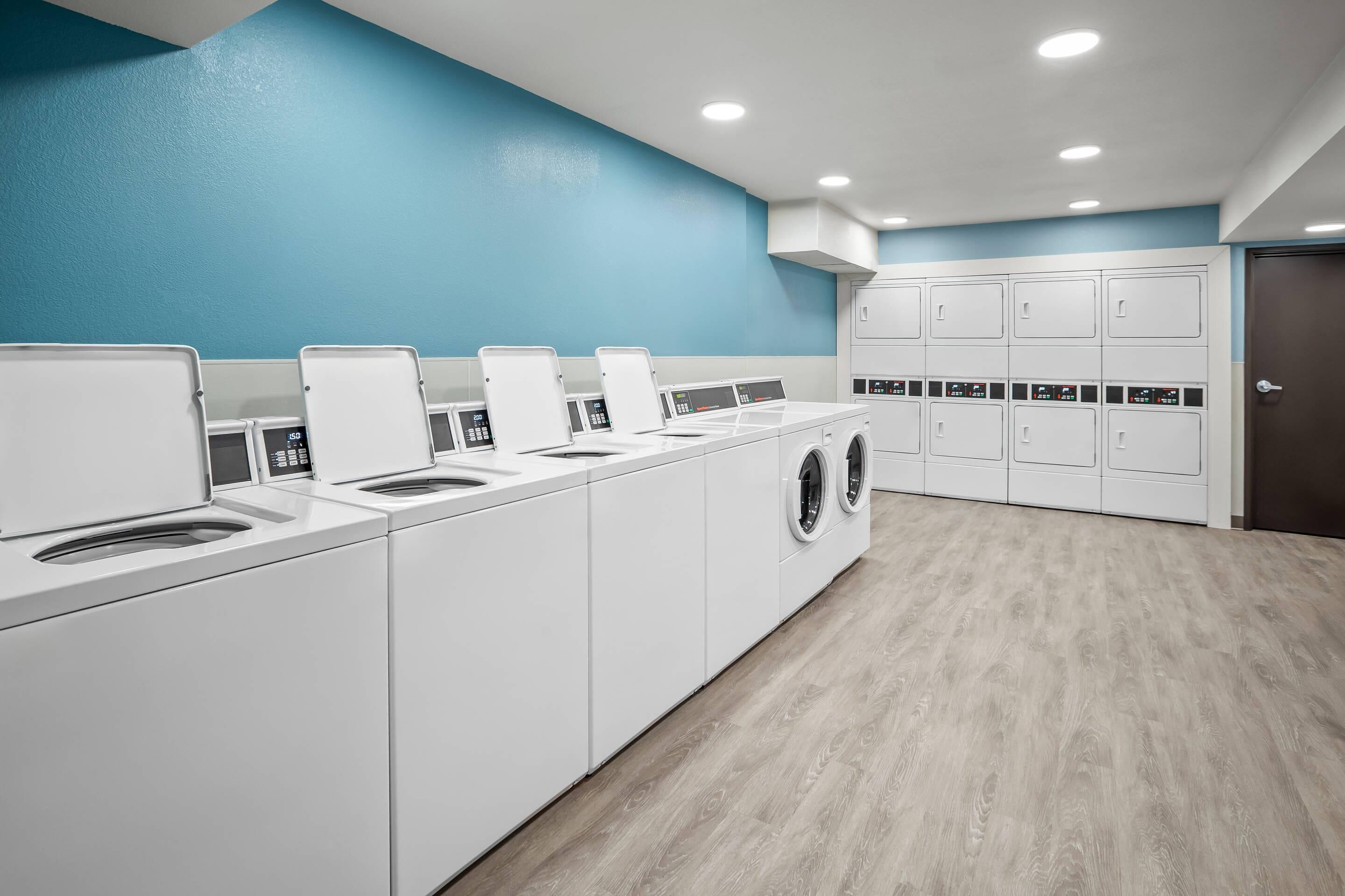 Un cuarto de lavandería con varias lavadoras y secadoras, una pared azul y piso de madera.