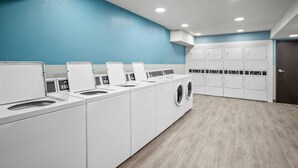 Un cuarto de lavandería con varias lavadoras y secadoras, una pared azul y piso de madera.