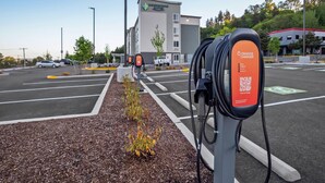 Un área de estacionamiento con estaciones de carga para vehículos eléctricos, un edificio de hotel al fondo y un cielo despejado.