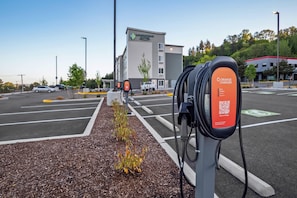 Een parkeerterrein met laadpalen voor elektrische voertuigen, een hotel op de achtergrond en een heldere lucht.