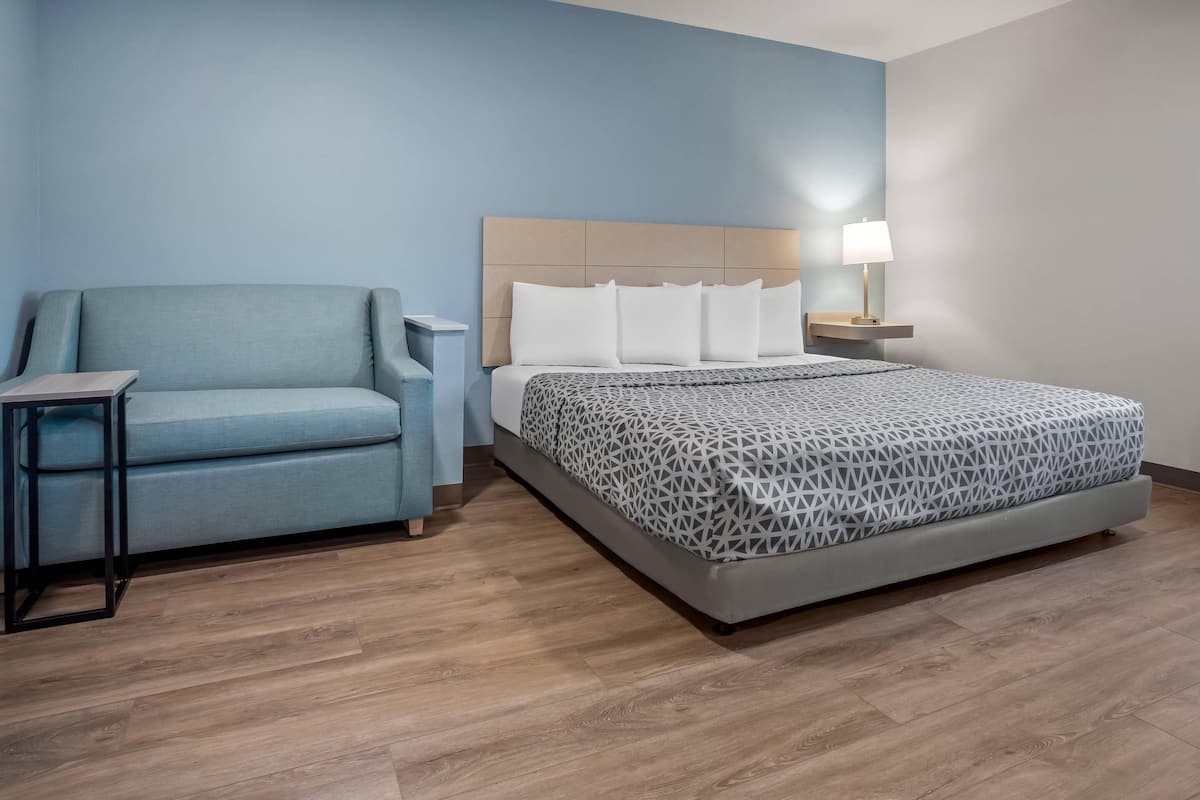 Een hotelkamer met een bed, een bank, een nachtkastje en een lamp.