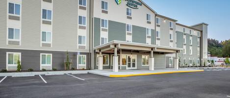 A multi-story hotel with a flat roof, a covered entrance, and a parking lot.