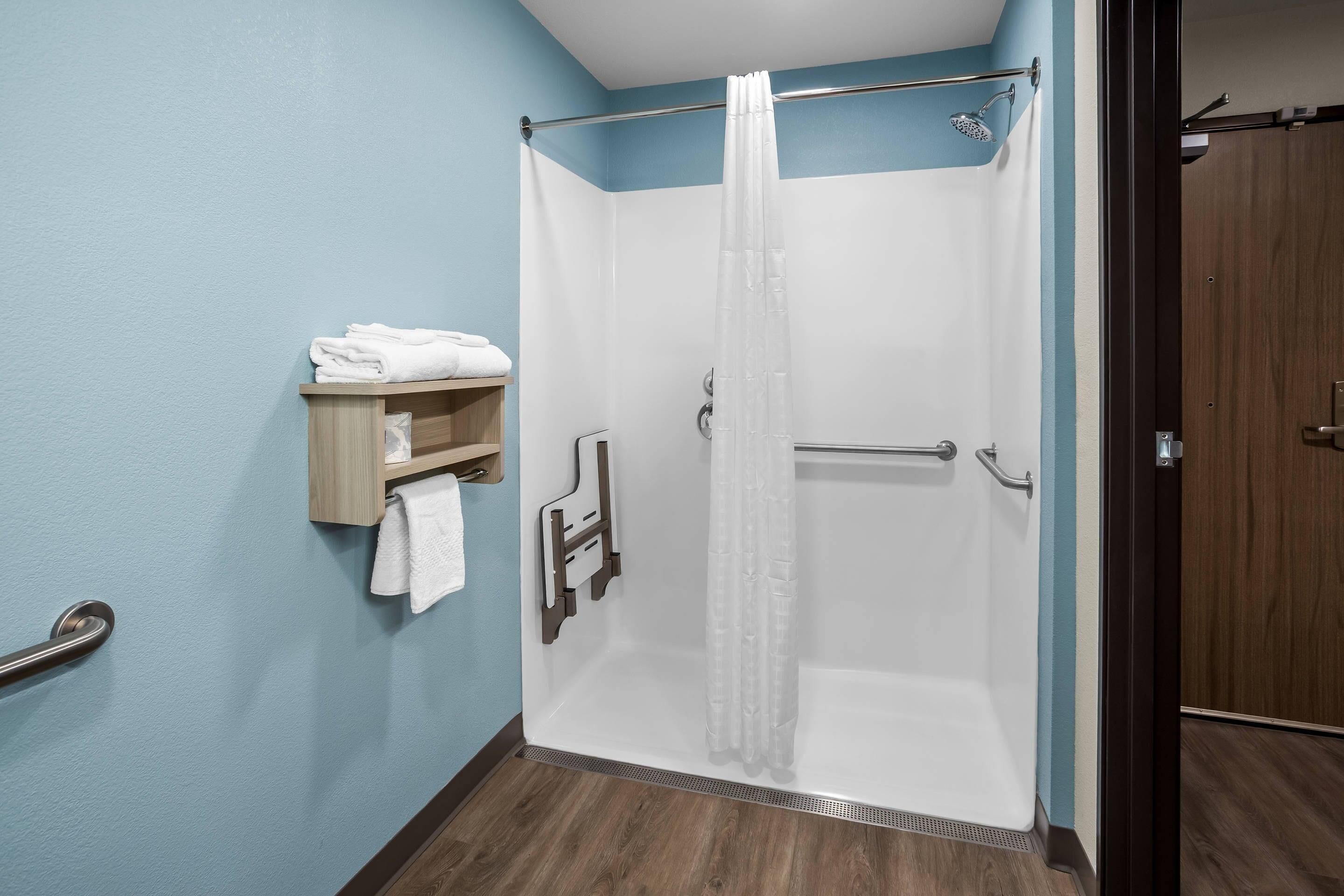 A shower with a glass door, a towel rack with folded towels, and a wooden shelf.