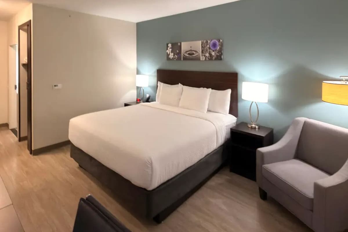 A hotel room with a large bed, bedside tables, a chair, and a wall-mounted artwork.