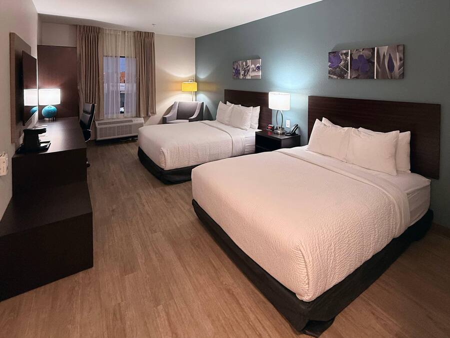 A hotel room with two beds, a desk, a chair, a lamp, and artwork on the walls.
