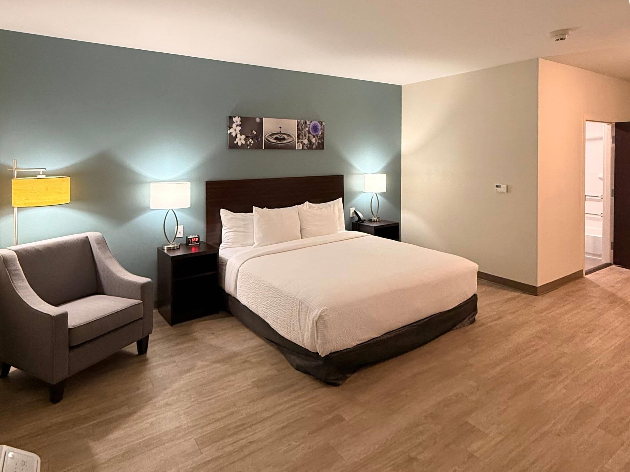 A hotel room with a large bed, two bedside tables with lamps, a chair, and a wall-mounted artwork.