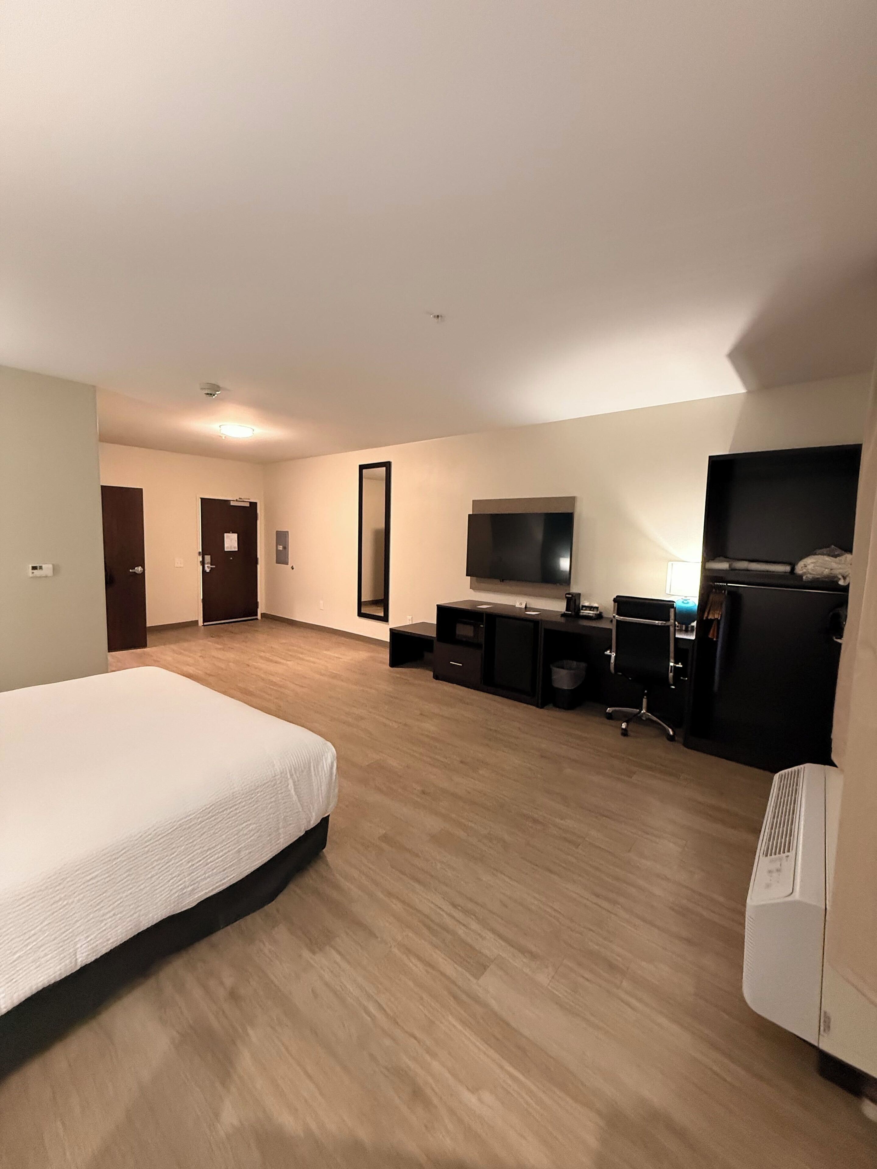 Una habitación de hotel con una cama, un escritorio con computadora, un televisor y un espejo grande.