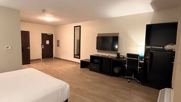 Una habitación de hotel con una cama, un escritorio con computadora, un televisor y un espejo grande.