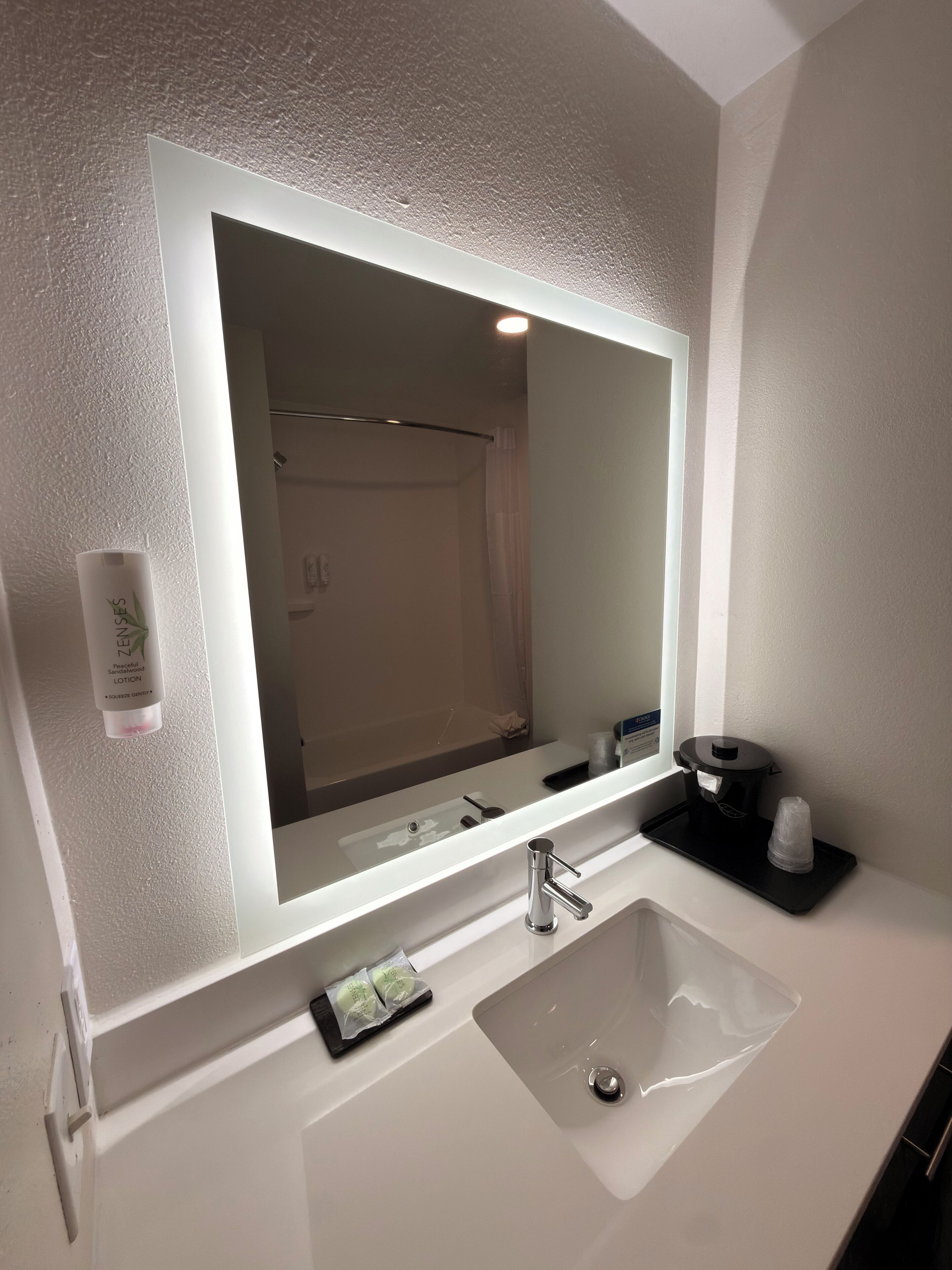 A bathroom with a large mirror, a sink, and a towel dispenser.