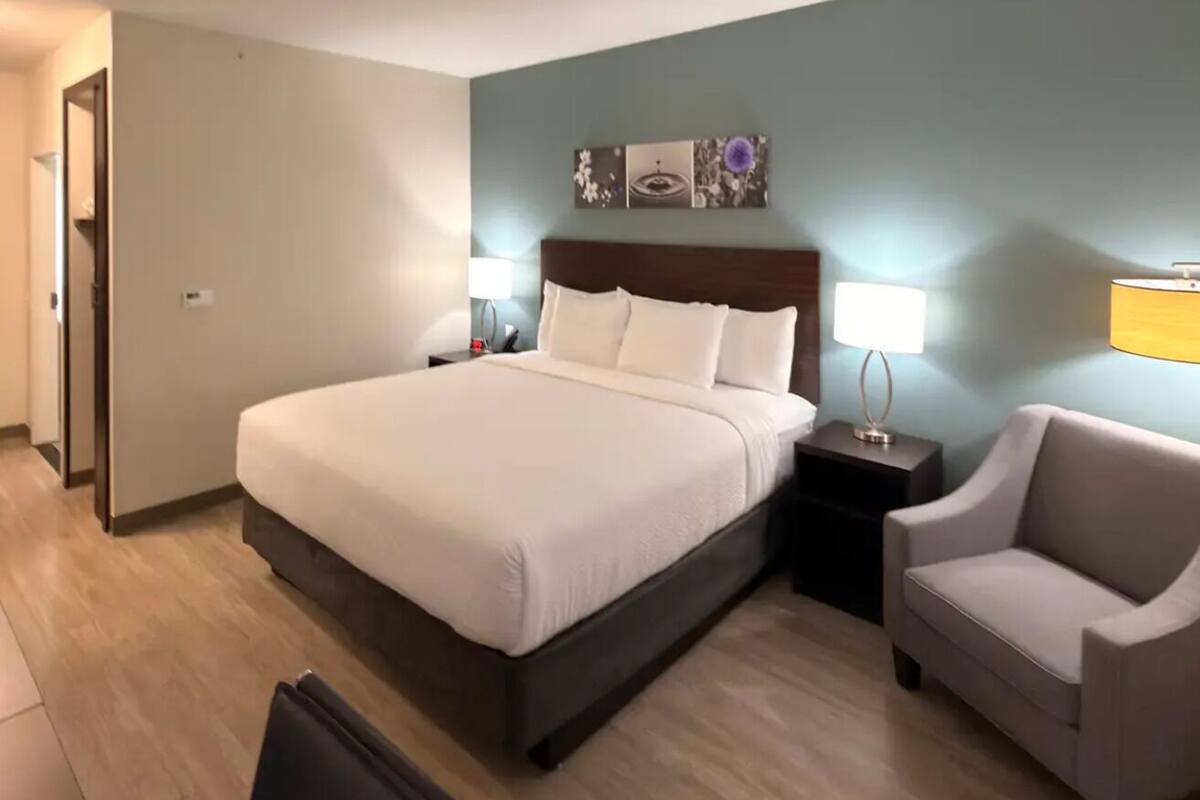 Une chambre d’hôtel avec un grand lit, des tables de chevet, une chaise et une œuvre d’art accrochée au mur.