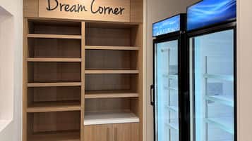 A room with a wooden shelving unit labeled "Dream Corner" and a glass-fronted refrigerator.
