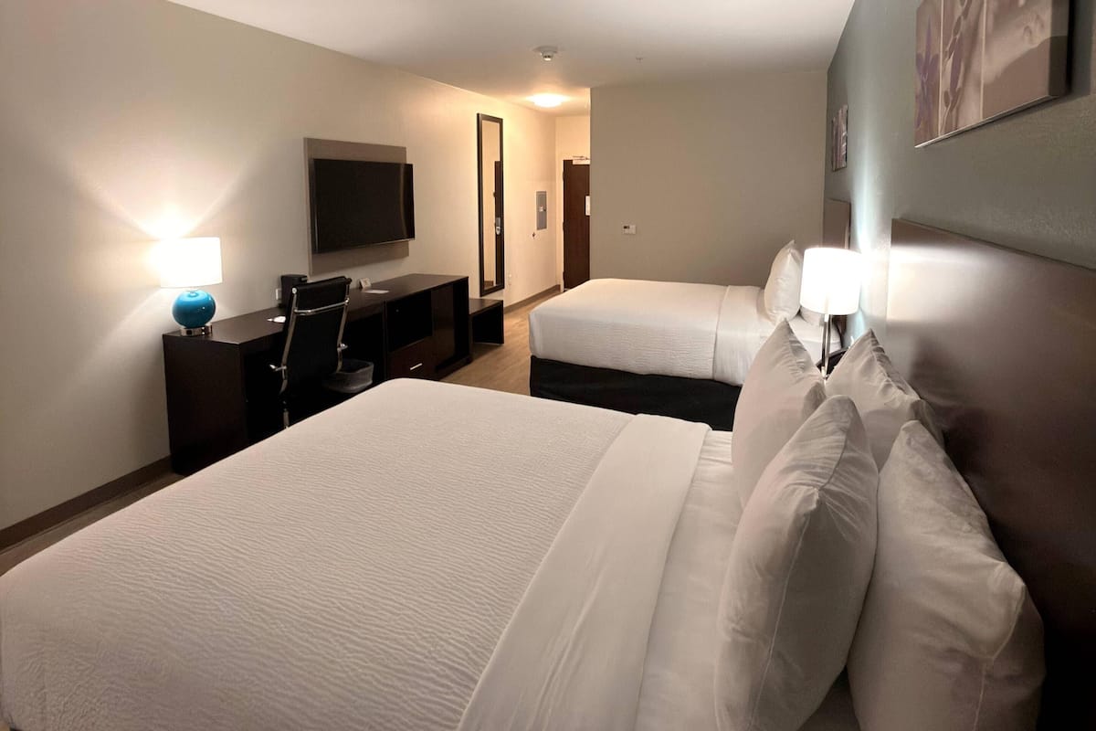 Une chambre d’hôtel avec un grand lit, un lit plus petit, un bureau avec une chaise, un téléviseur à écran plat fixé au mur et une lampe sur le bureau.