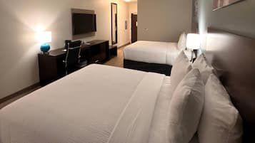 A hotel room with a large bed, a smaller bed, a desk with a chair, a flat-screen TV mounted on the wall, and a lamp on the desk.