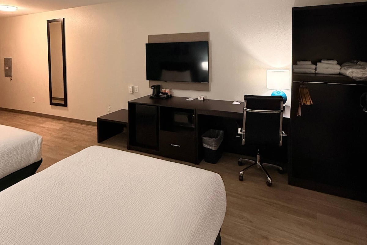 Une chambre d’hôtel avec deux lits, un bureau avec un ordinateur, une télévision et une armoire.