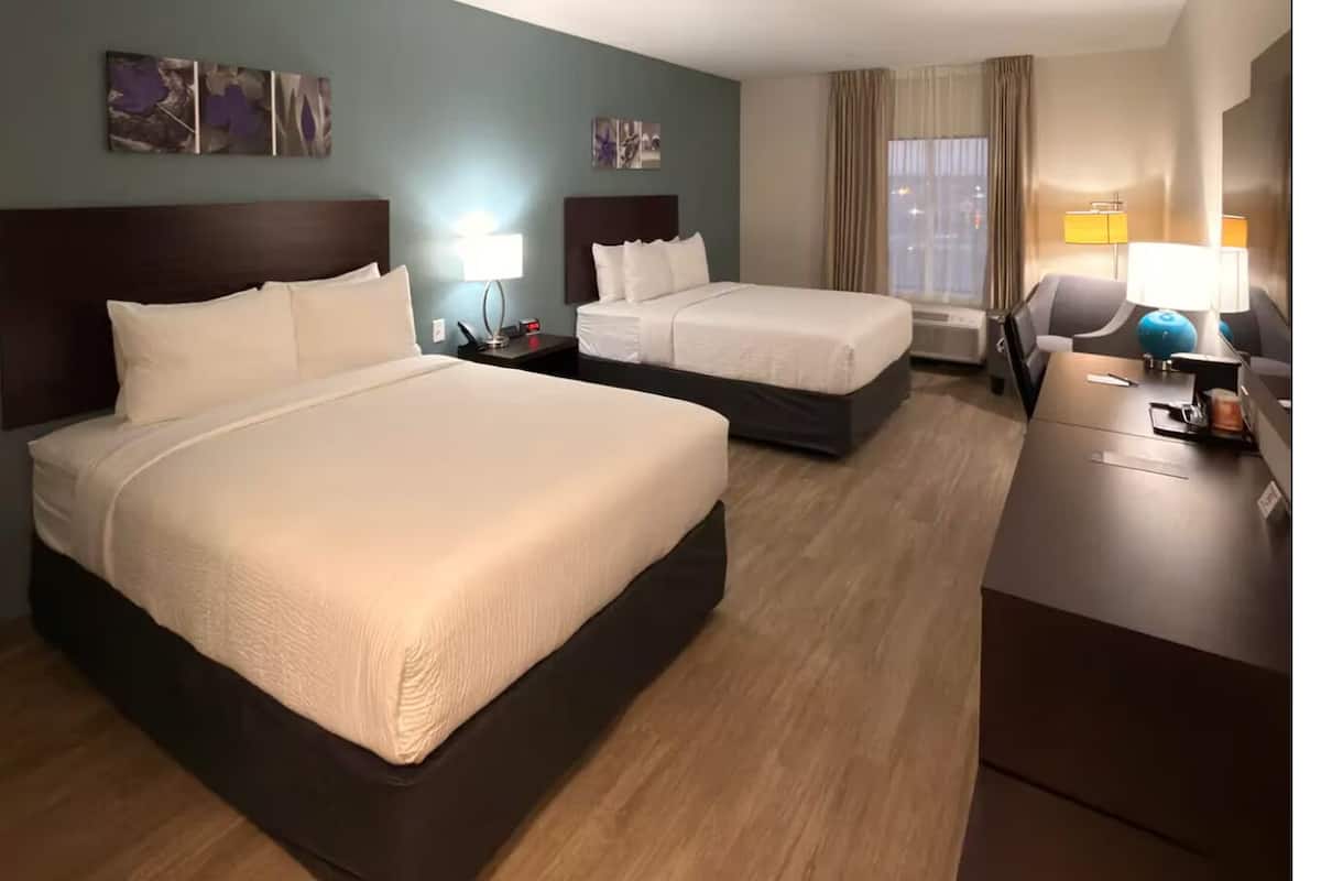 Une chambre d’hôtel avec deux lits, un bureau, une chaise, une lampe et des œuvres d’art accrochées aux murs.