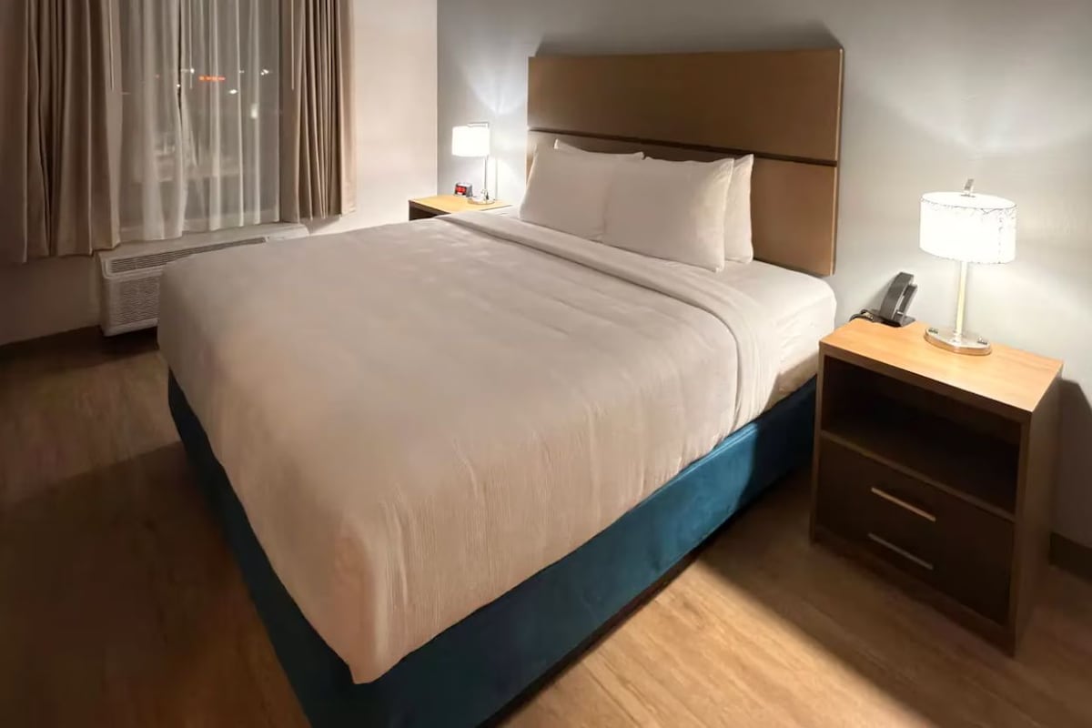 A hotel room with a bed, bedside tables, a lamp, and a nightstand.