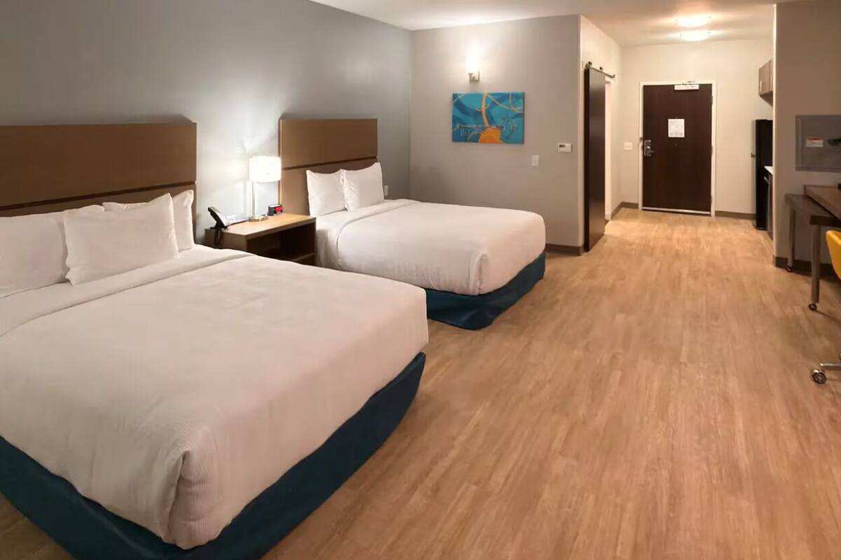 Une chambre d’hôtel avec deux lits, un bureau, une chaise, une lampe, un tableau et une porte.