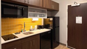 A compact kitchen with wooden cabinets, a microwave, a refrigerator, and a dishwasher. - Mainstay Suites - Oklahoma City Airport (Oklahoma City)