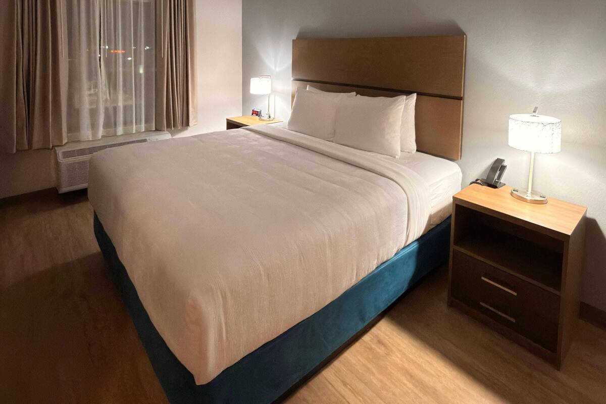 Une chambre d’hôtel avec un lit, des tables de chevet, une lampe et une fenêtre avec des rideaux.