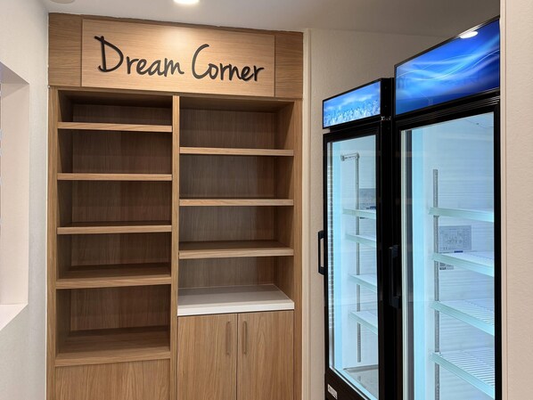A room with a wooden shelving unit labeled "Dream Corner" and a glass-fronted refrigerator. - Mainstay Suites - Oklahoma City Airport (Oklahoma City)