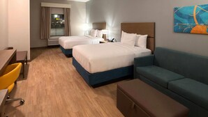 A hotel room with two beds, a desk, a chair, a sofa, and a painting on the wall. - Mainstay Suites - Oklahoma City Airport (Oklahoma City)