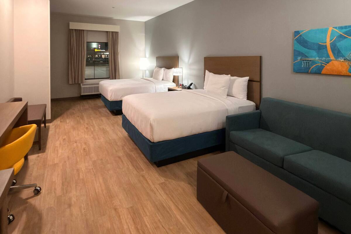 Une chambre d’hôtel avec deux lits, un bureau, une chaise, un canapé et un tableau au mur.