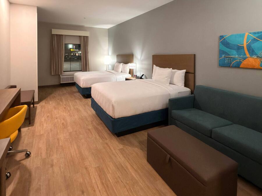 A hotel room with two beds, a desk, a chair, a sofa, and a painting on the wall.