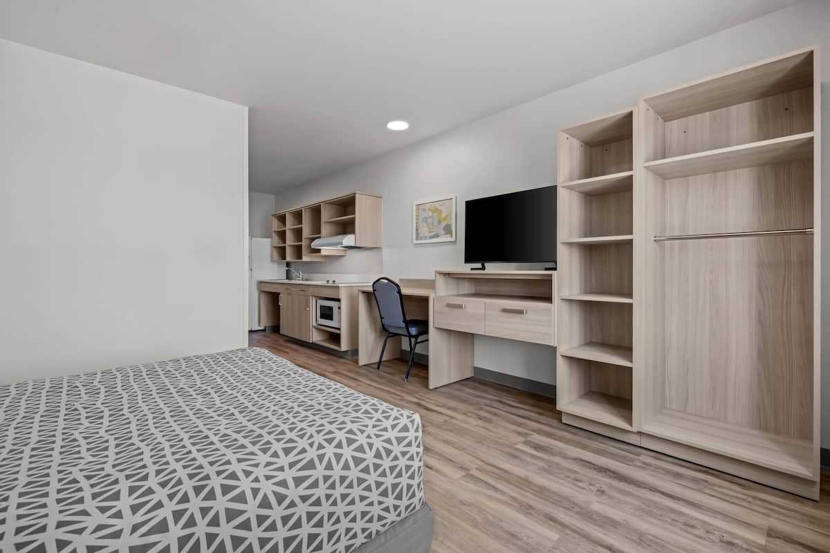 Un dormitorio moderno con cama, escritorio, silla, televisor y estanterías empotradas.
