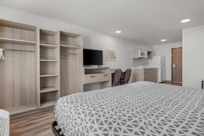 A bedroom with a large bed, a TV, a desk with chairs, a wardrobe, and a kitchenette. - Woodspring Suites Manteca - Stockton South (Manteca)