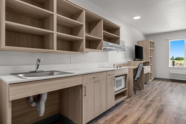 A modern kitchen with built-in cabinets, a sink, and a flat-screen TV. - Woodspring Suites Manteca - Stockton South (Manteca)
