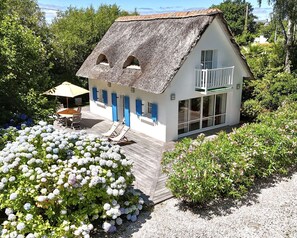A house with a thatched roof, a balcony, and a wooden deck with outdoor furniture. - La Petite Maison du Caillou, a typical 3-star Breton house with a thatched roof (FOUESNANT)