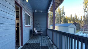 En træterrasse med en gyngestol, et overdækket område og udsigt til et sneklædt landskab med træer.