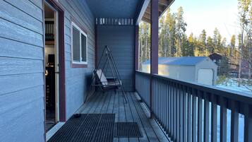 Une véranda en bois avec une chaise suspendue, un espace abrité et une vue sur un paysage enneigé parsemé d’arbres.