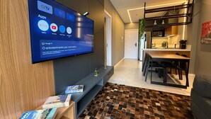 Ein modernes Wohnzimmer mit einem an der Wand befestigten Flachbildfernseher, der verschiedene Streaming-Apps anzeigt. Im Raum steht eine Holzbank mit Büchern und ein gemustertes Teppich. Im Hintergrund ist ein Essbereich mit Tisch und Stühlen zu sehen.