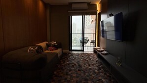 Ein modernes Hotelzimmer mit einer Couch, einem Flachbildfernseher, einem gemusterten Boden und Blick auf die Stadt durch ein großes Fenster.