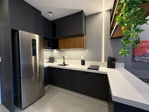 Eine moderne Küche mit dunklen Schränken, einem Edelstahlkühlschrank, einer eingebauten Mikrowelle und einer schwarzen Induktionskochplatte.