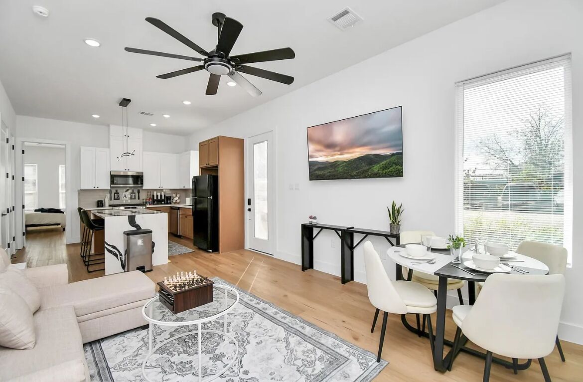 Una cocina moderna con una isla central, un comedor con mesa y sillas, una sala de estar con sofá y mesa de centro, y un ventilador de techo.