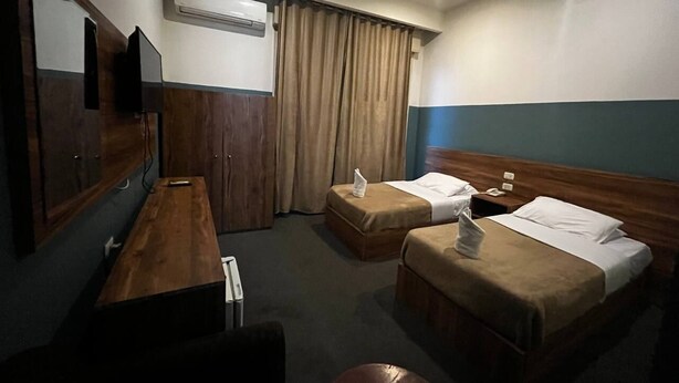Hotellihuone, jossa on kaksi sänkyä, puinen työpöytä, litteänäyttöinen televisio ja ilmastointilaite.