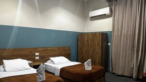 Hotellihuone, jossa on kaksi sänkyä, vaatekaappi, ilmastointilaite ja verho.