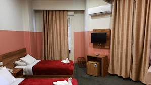 Hotellihuone, jossa on kaksi sänkyä, seinälle asennettu televisio, ilmastointilaite ja puinen yöpöytä.