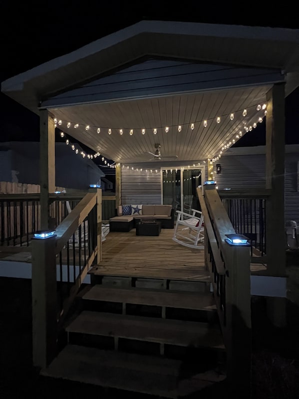 A covered outdoor deck with string lights, a seating area with cushions, and a wooden railing. - Charming Coastal Cottage in Historic Downtown Summerville (Summerville)