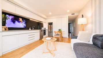 A modern kitchen with a flat-screen TV, wooden flooring, and a dining area with a table and chairs.