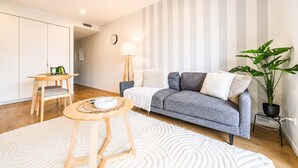 A modern living room with a grey sofa, a round wooden coffee table, a white rug, a floor lamp, and a potted plant. - Sydenham | Patio + Free Parking Near CBD (Christchurch)