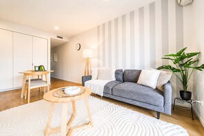 A modern living room with a grey sofa, a round wooden coffee table, a white rug, a floor lamp, and a potted plant. - Sydenham | Patio + Free Parking Near CBD (Christchurch)