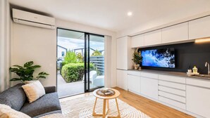 A modern living room with a sofa, a coffee table, and a TV mounted on the wall. - Sydenham | Patio + Free Parking Near CBD (Christchurch)